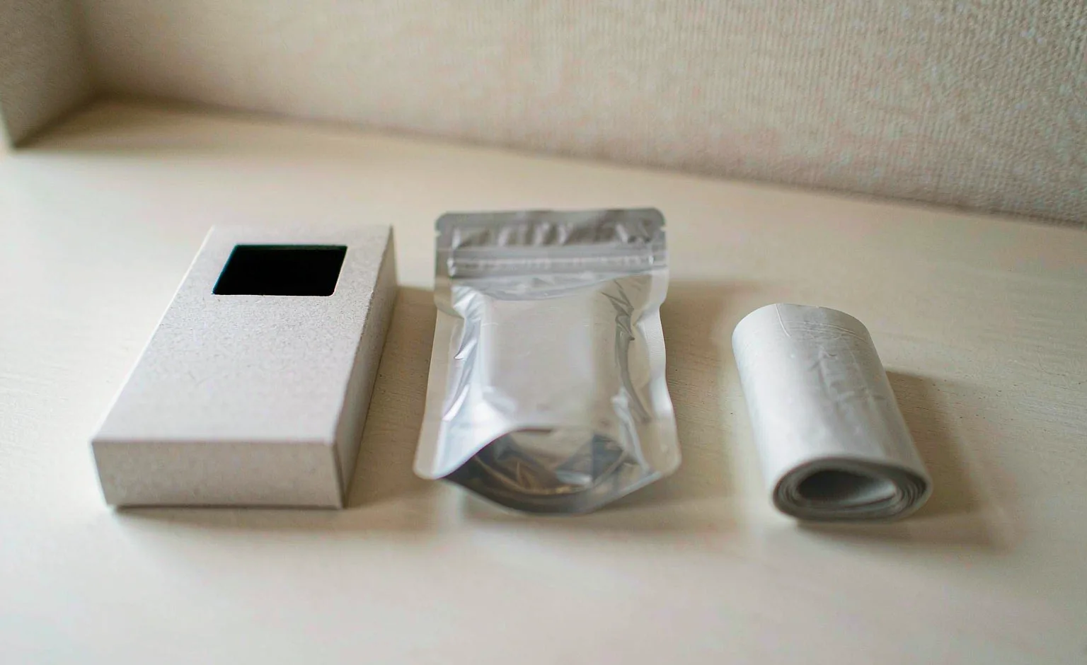 A flat carton, a soft film pouch and a rolled pack arranged side by side on a plain surface.